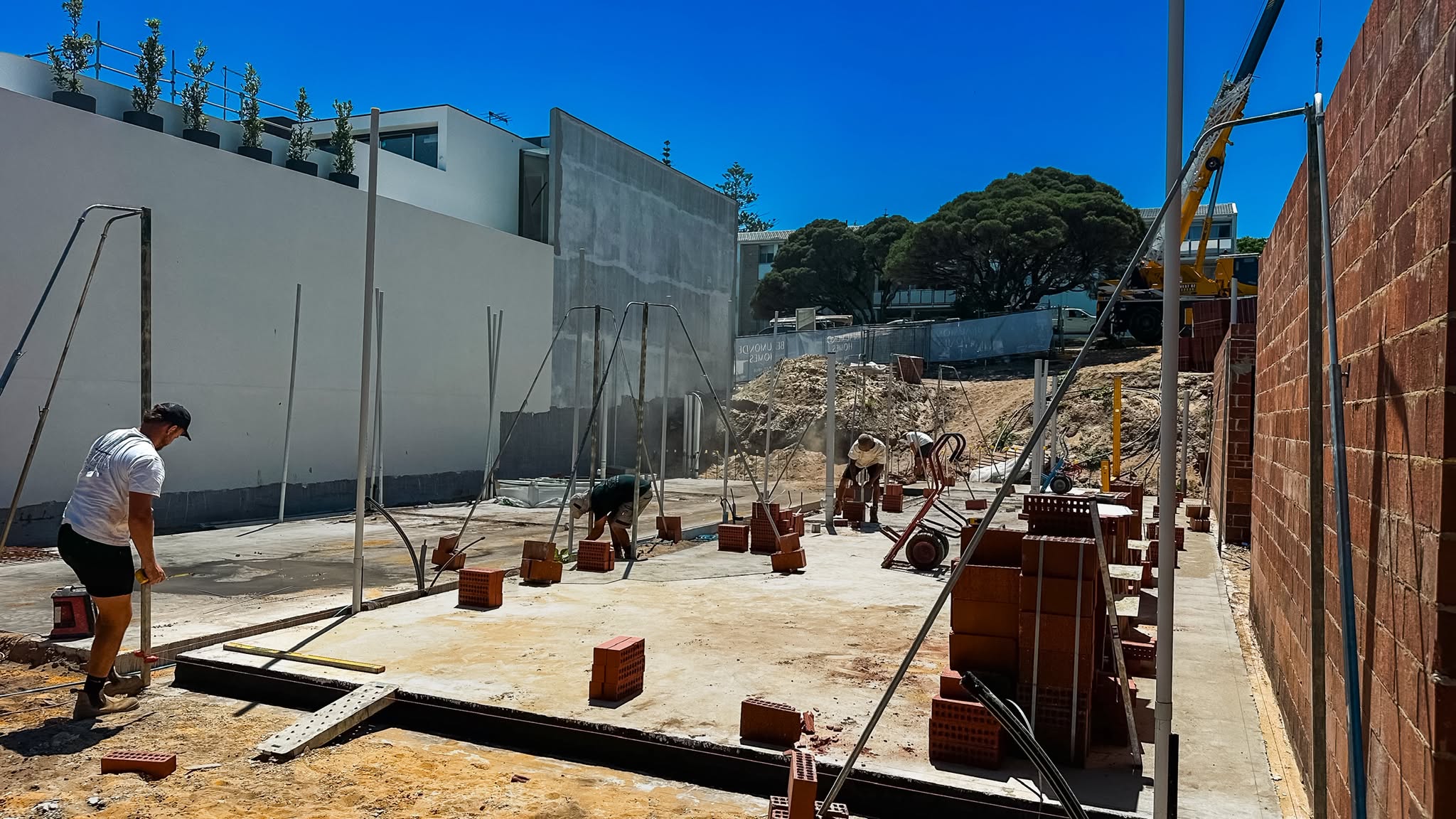 Bricklayer working on site beside a rendered wall and stacked brick packs