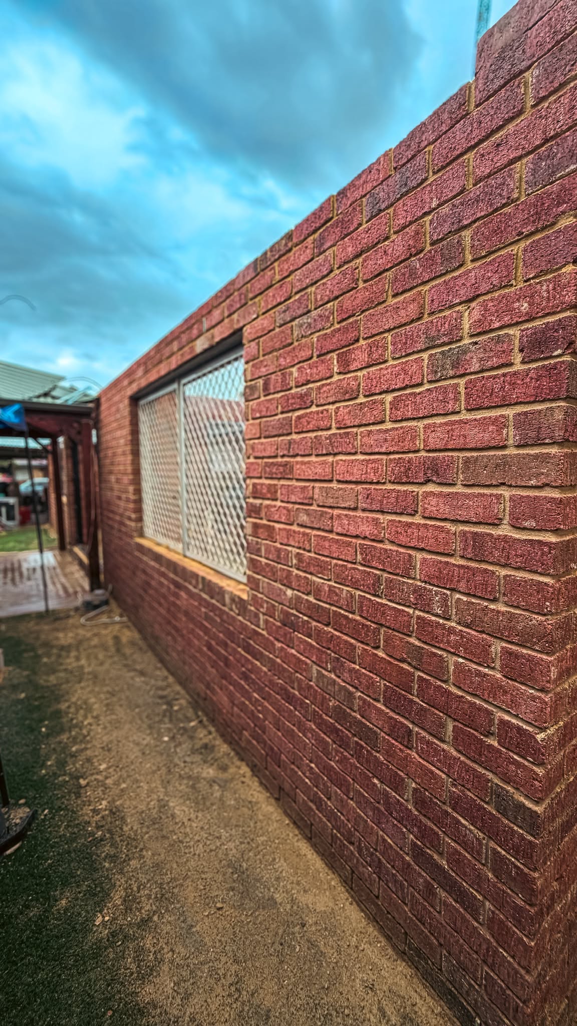 Long red brick wall running beside a path with a recessed feature panel